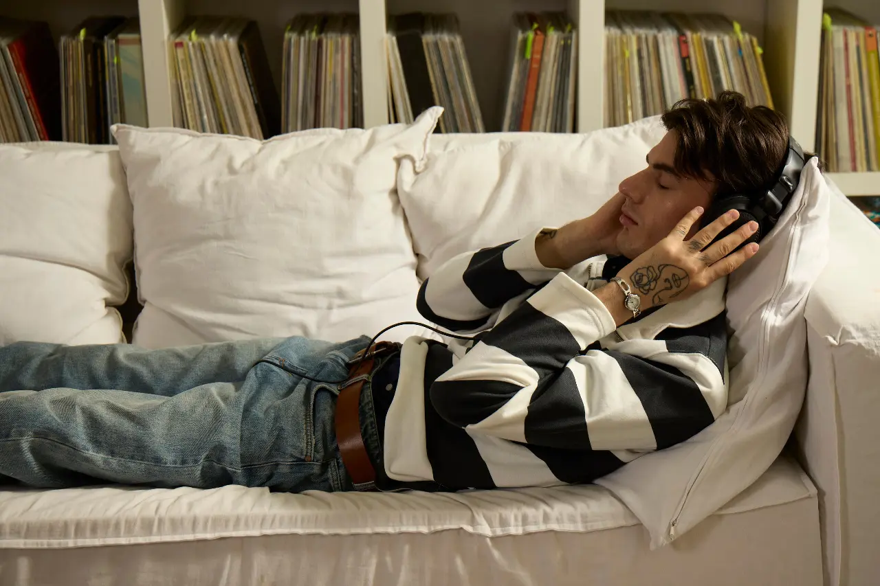 Person listening through headphones while reclining beside shelves of records