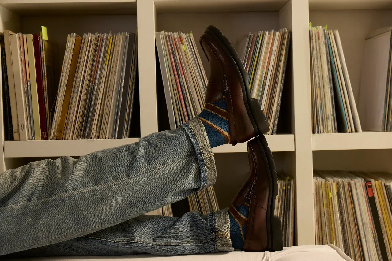 Brown loafers resting near a wall of organized vinyl records