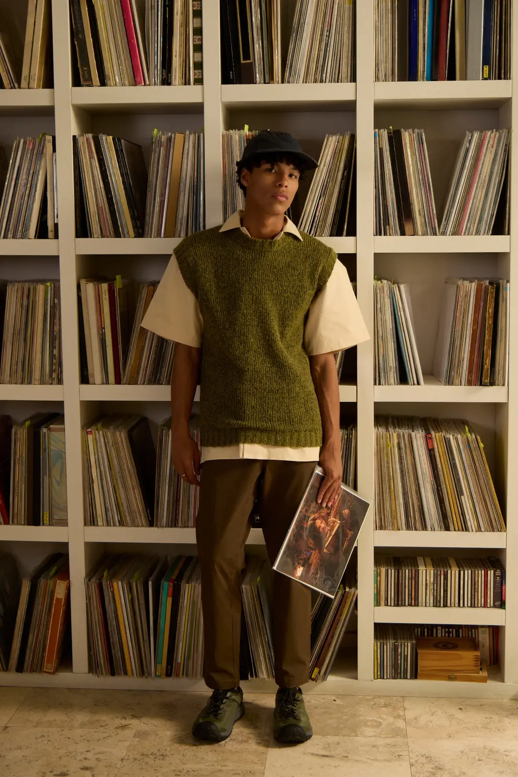 Person holding a vinyl record sleeve in front of a large record collection