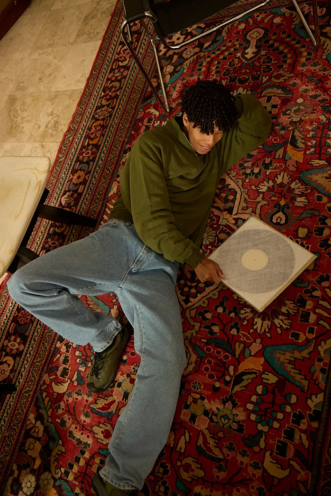 Overhead view of a person seated on a patterned rug with a vinyl record